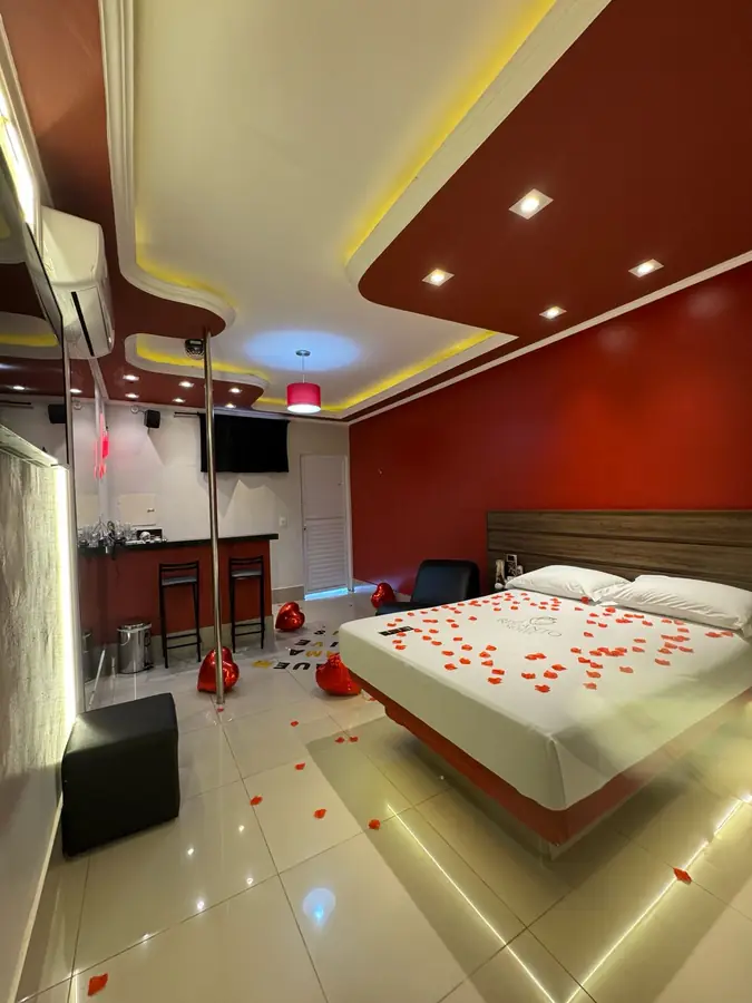 Cama king com pétalas de rosa e iluminação romântica no Recanto Motel